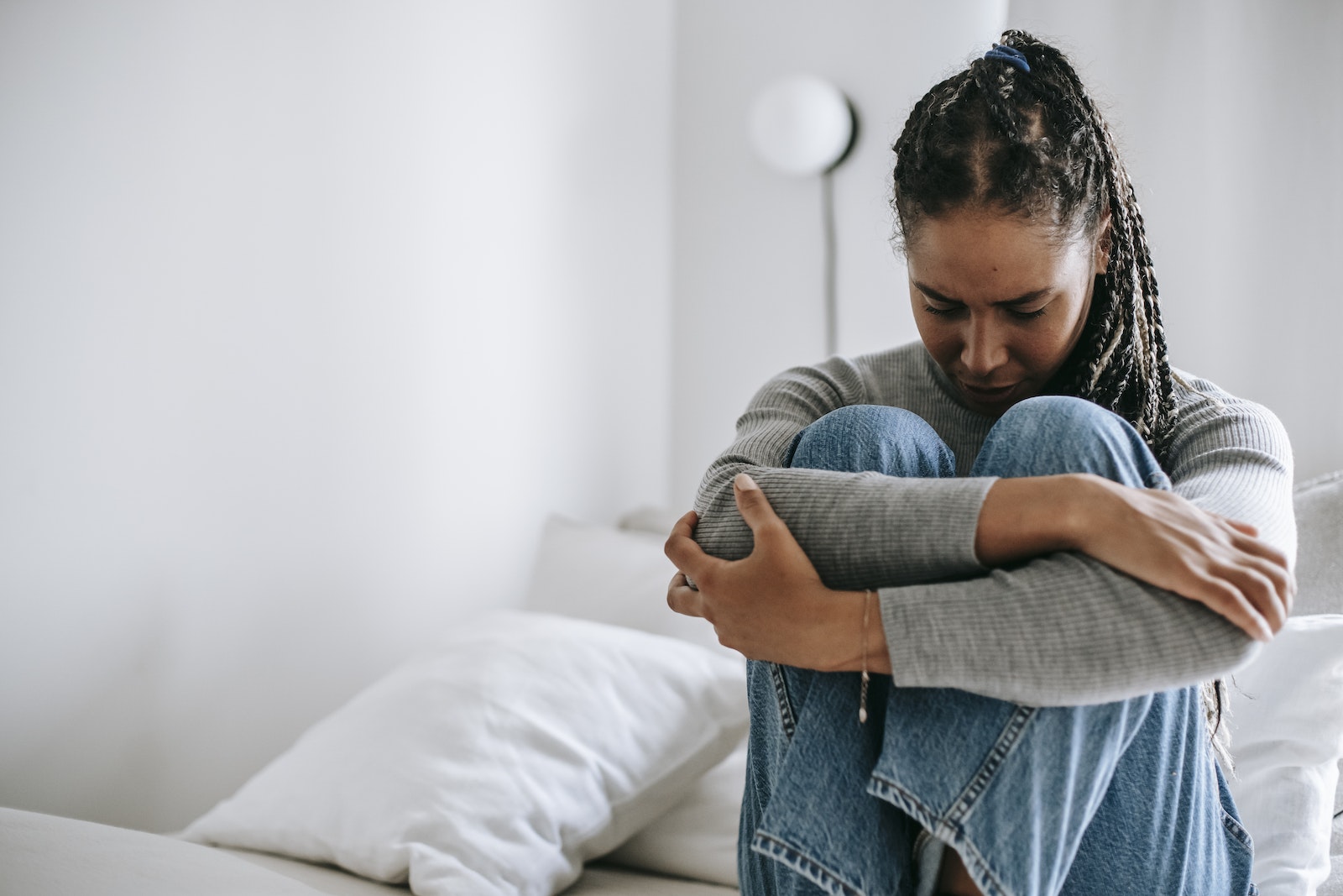 Upset ethnic woman embracing knees on bed