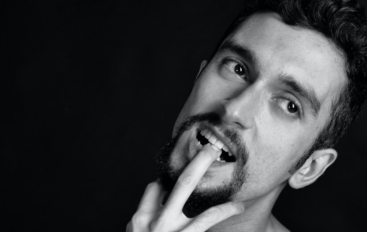 grayscale photography of man biting his finger